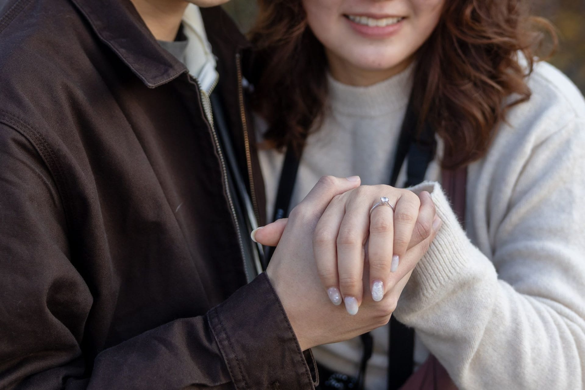 Close-up of a couple holding hands after a proposal at Lake Bled, showing the engagement ring on her finger — photographed by Damian Pristov.