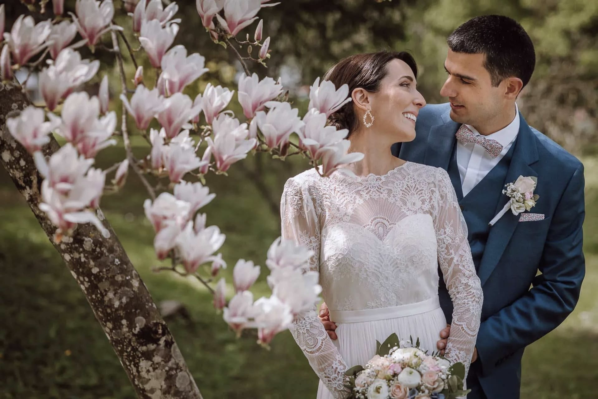 Bride and groom smile at each other under blooming magnolia blossoms during a spring wedding at Lake Bled.