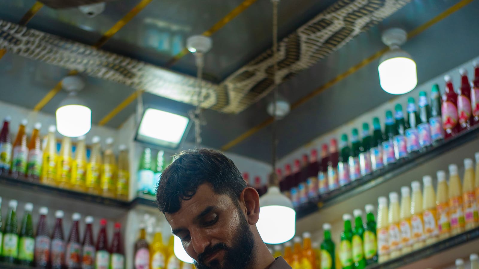 A shopkeeper in Karachi arranging his shop, with drinks and dried fruit on the shelves