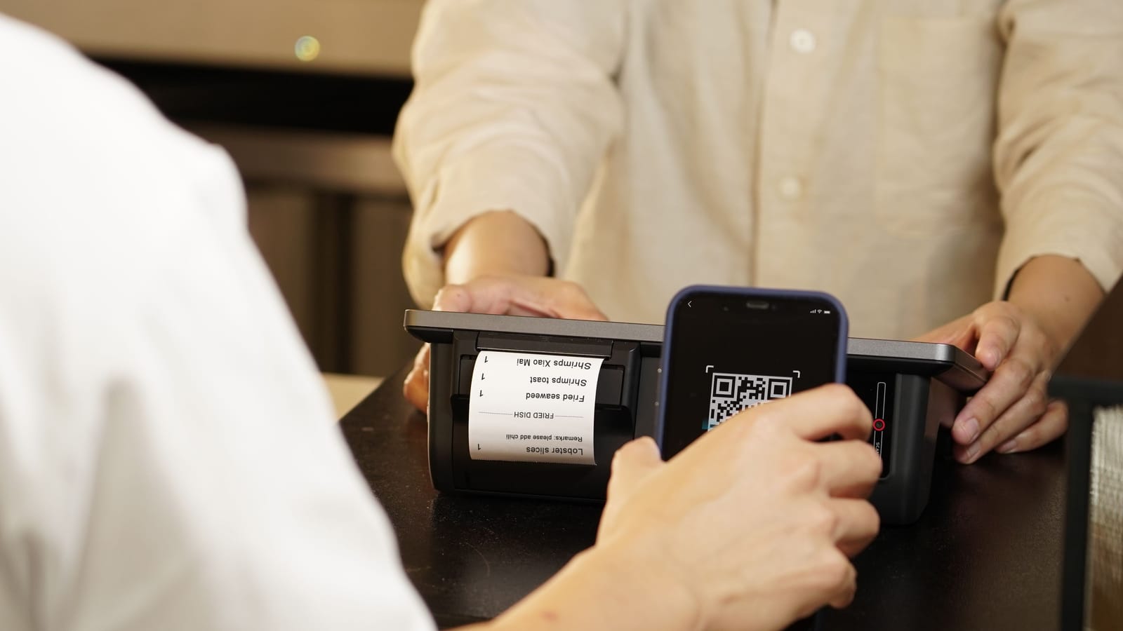 A customer paying at a shop counter by scanning a QR code with a phone