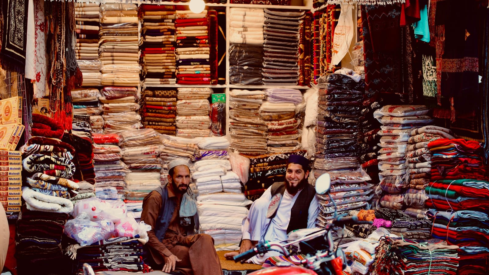 Two shopkeepers in Lahore smiling among stacks of fabric