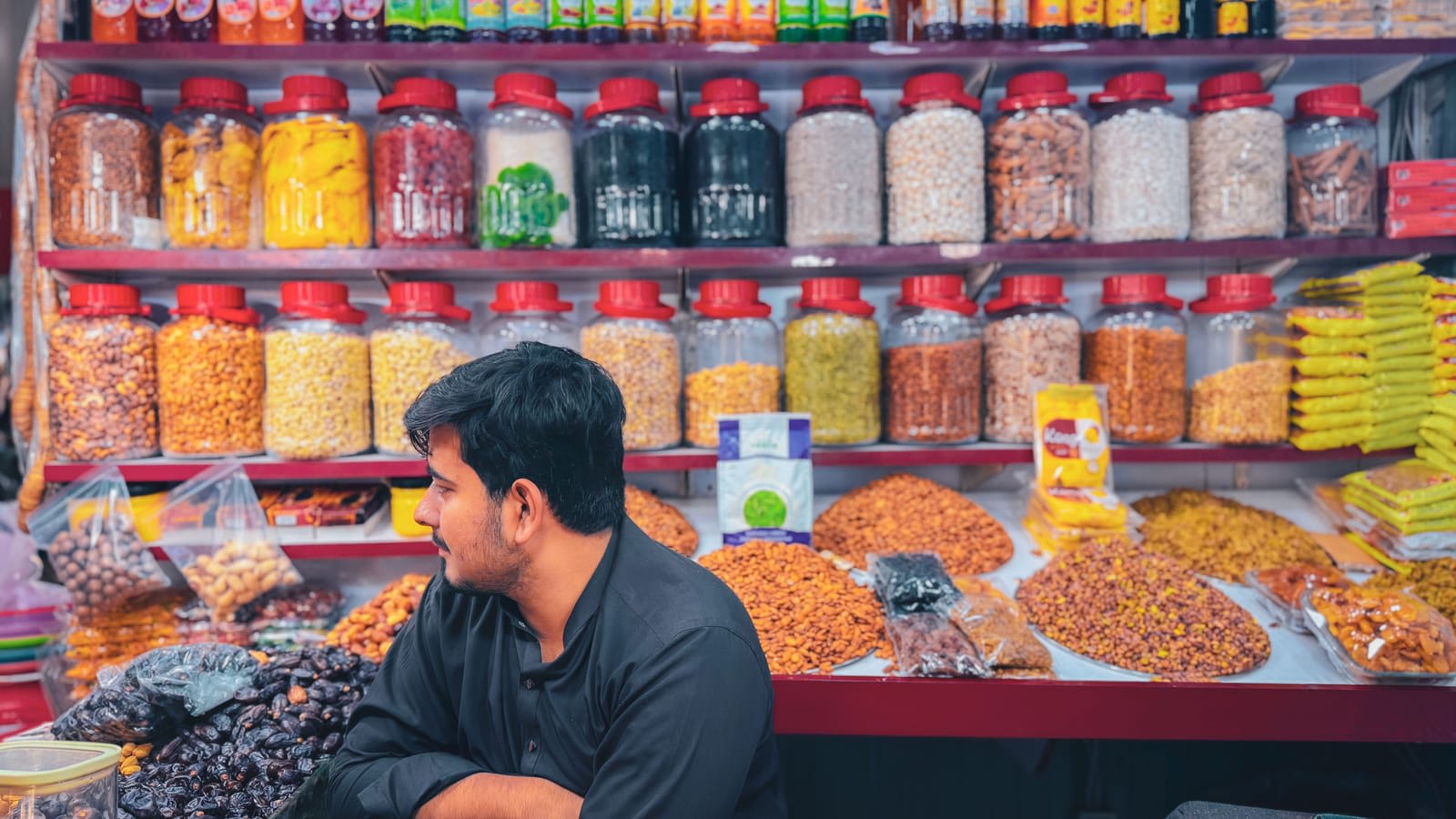 A shopkeeper among jars of spices, nuts and dried goods at his stall