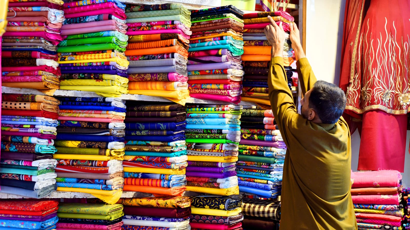 A cloth merchant in Multan stacking bolts of coloured fabric