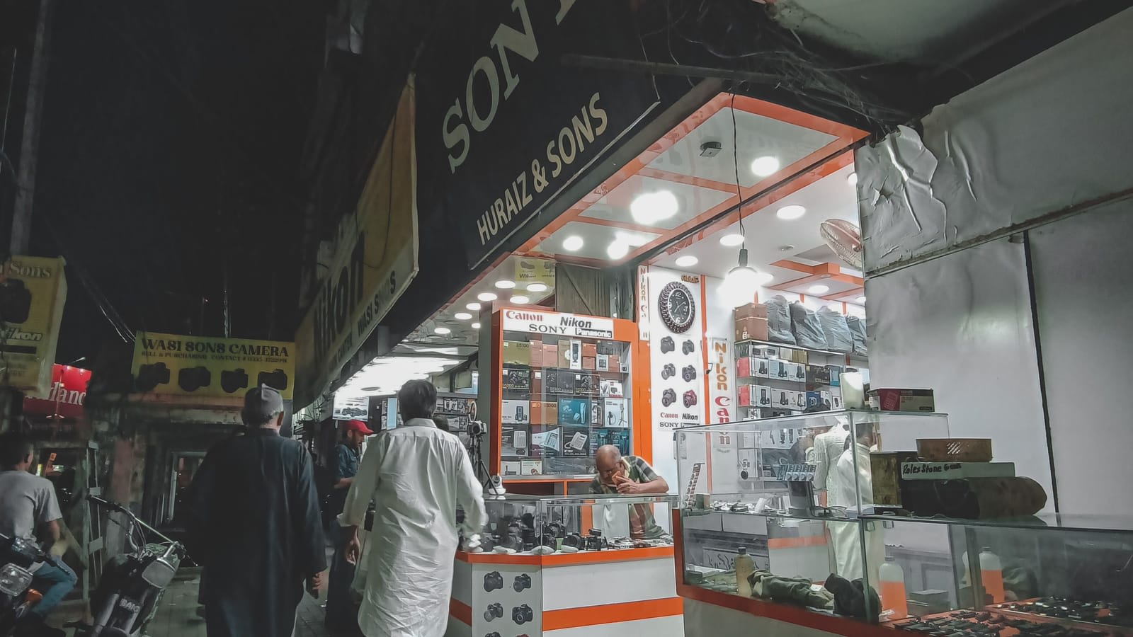 A row of electronics shops on a busy street in Karachi at night