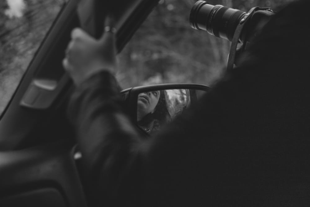 Black and white photograph of a photographer shooting from a car window