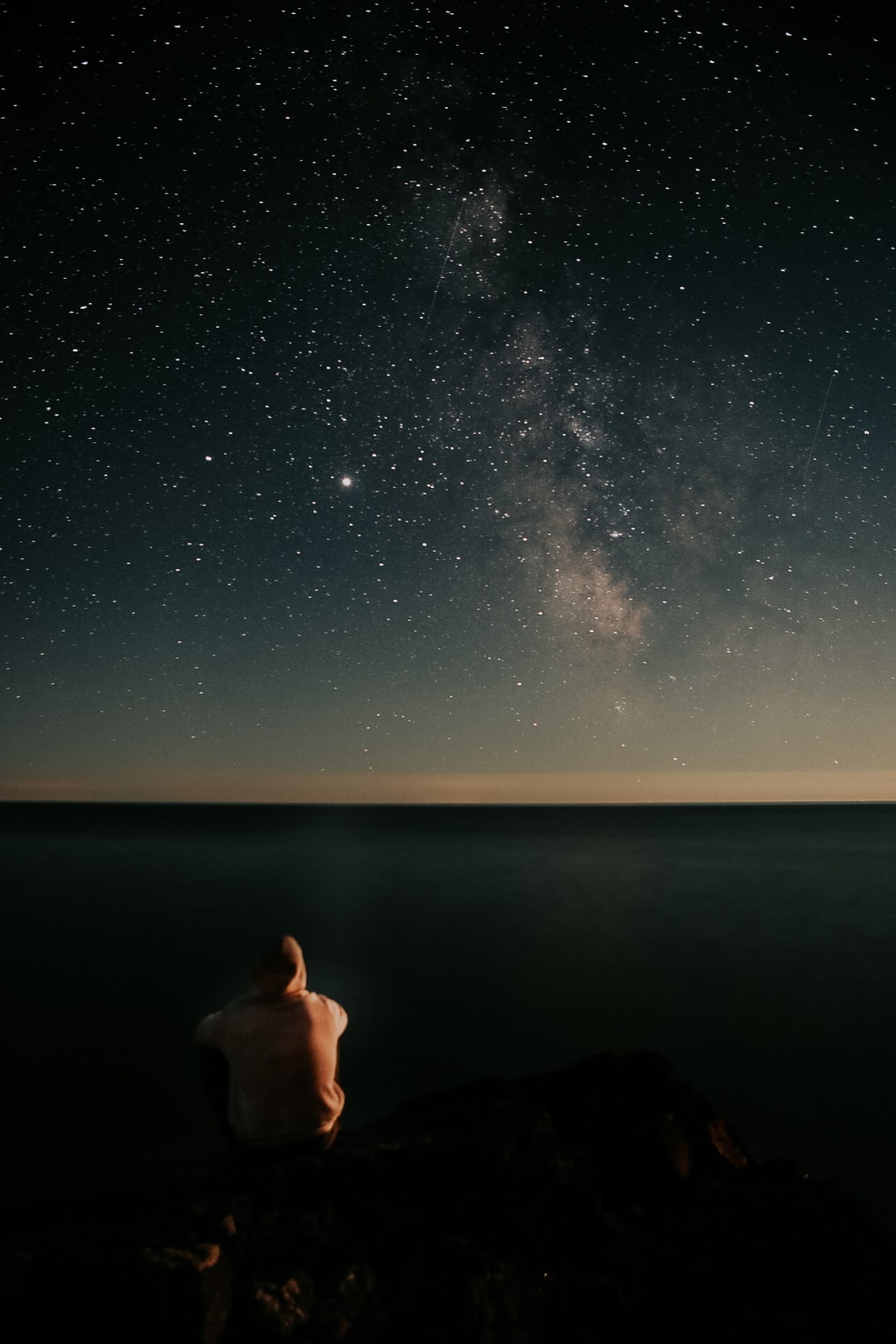 The Milky Way arcing over Lake Superior with a lone figure on the rocks below