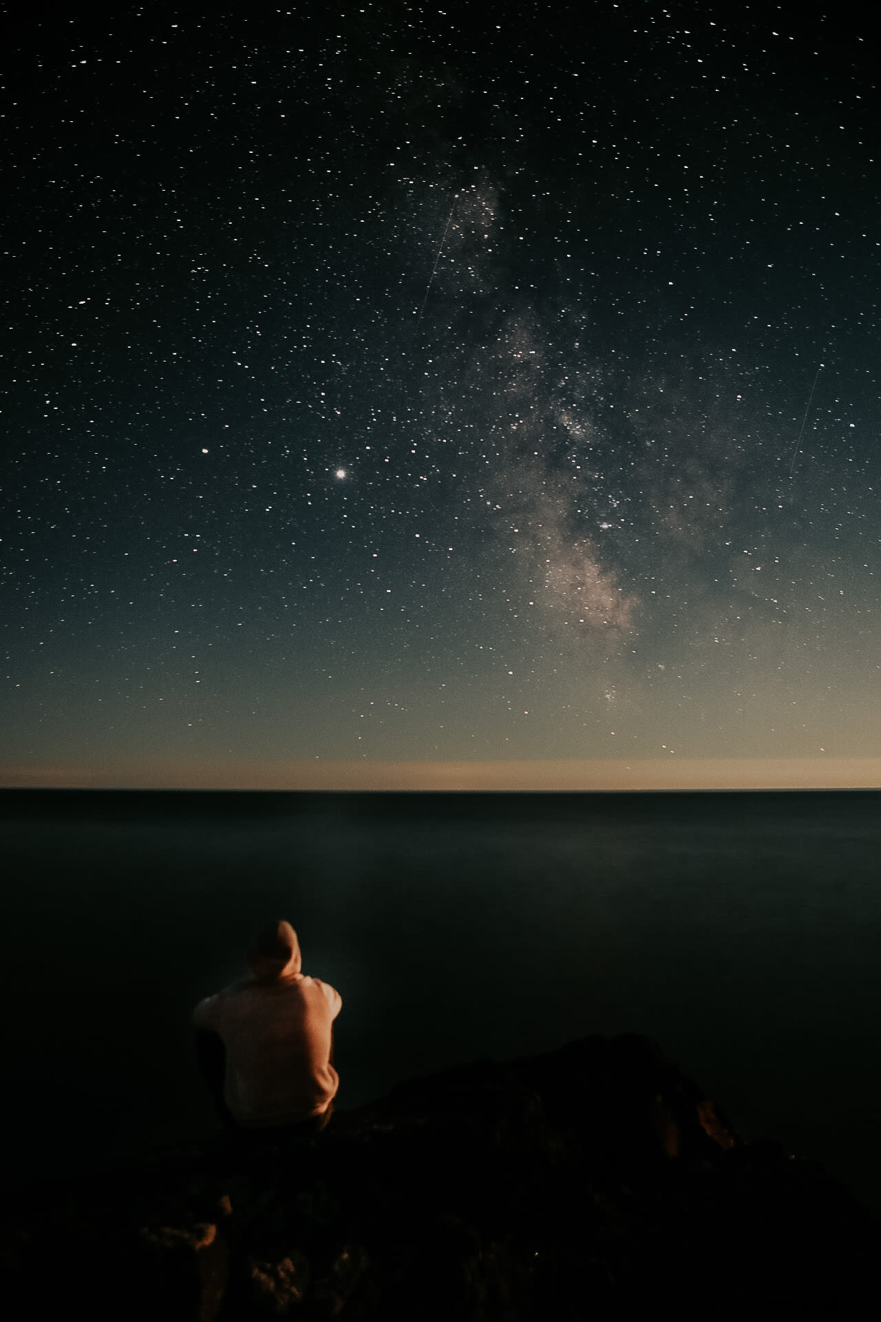 The Milky Way arcing over Lake Superior with a lone figure on the rocks below