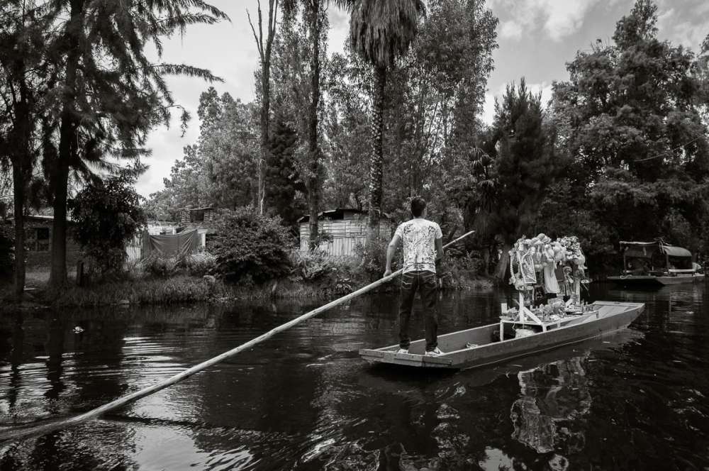 Young man using pole to move his boat through the canals at Xochimilco.