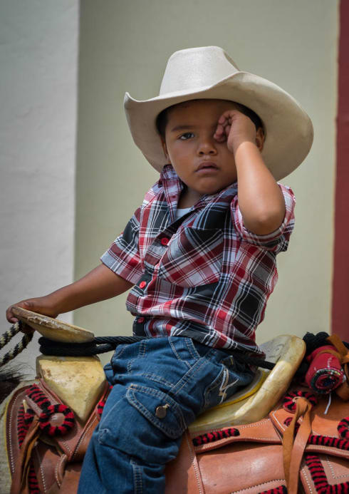 A young cowboy wipes the sleep from his eyes while waiting for mass to end on the Day of the Cowboy.