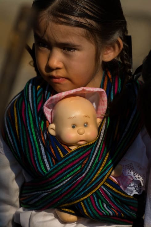 Girls sometimes march with a baby doll wrapped in a rebozo.