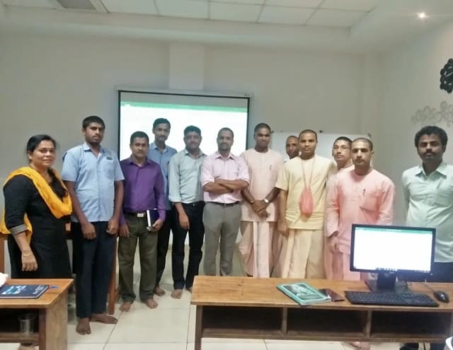 A group standing together in front of a projection screen, with a computer on the desk in front of them