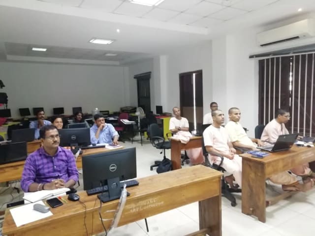 People seated at desktop computers in a computer lab, with rows of monitors behind them