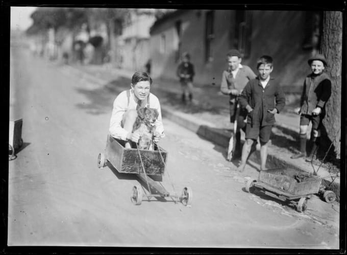 Boy and dog in a billycart race past other children on a suburban street, Sydney, ca. 1920s.