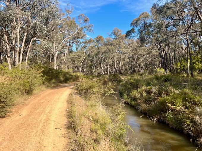 An unsealed road following a water channel