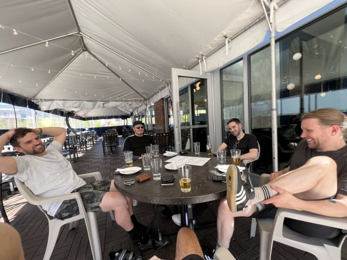 Five friends around an outdoor table enjoying a beer