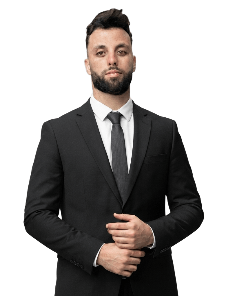 Imad, photographed in a black suit and dark tie, hands clasped.