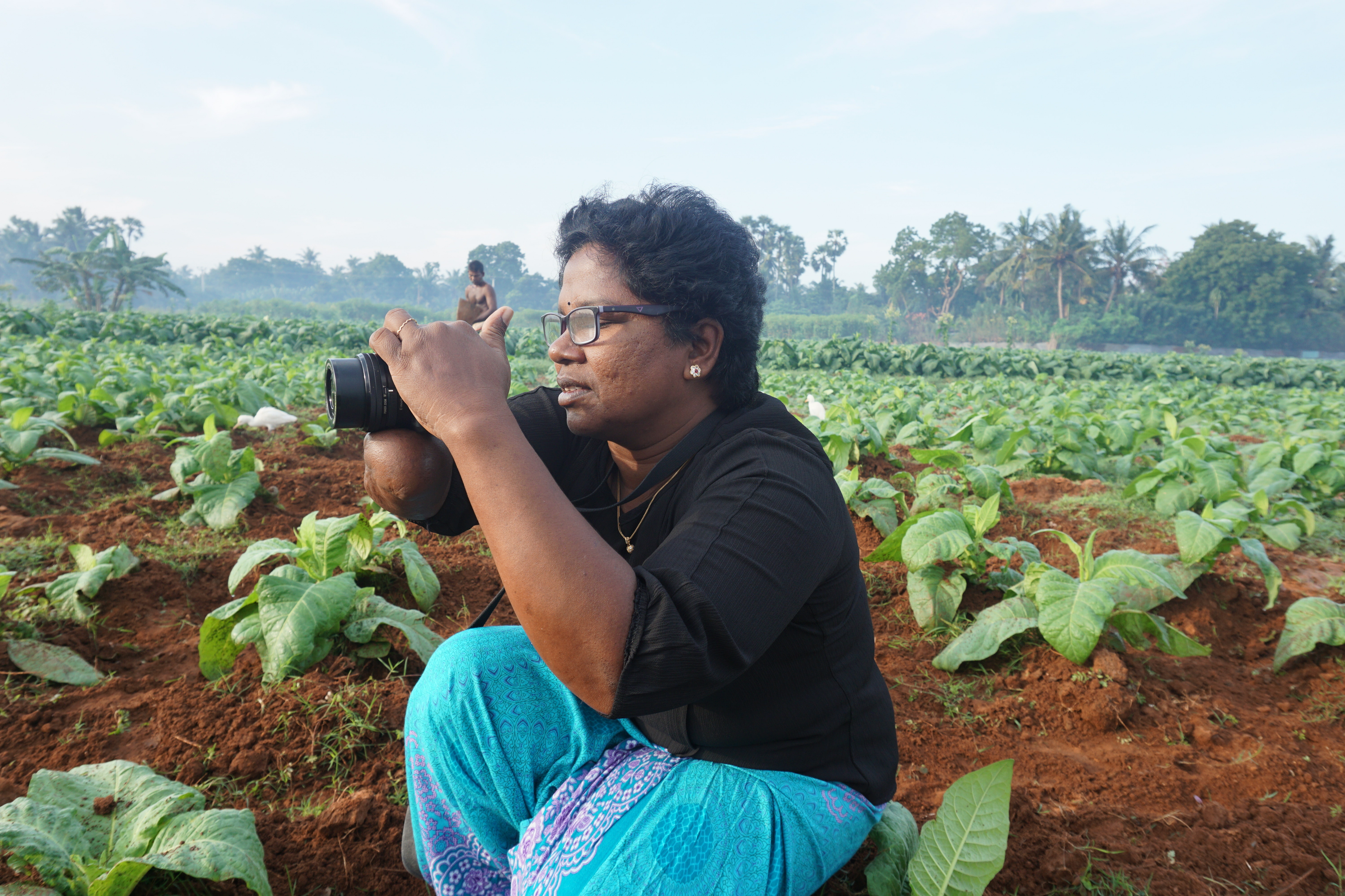 Woman in field of green crops taking a photo.