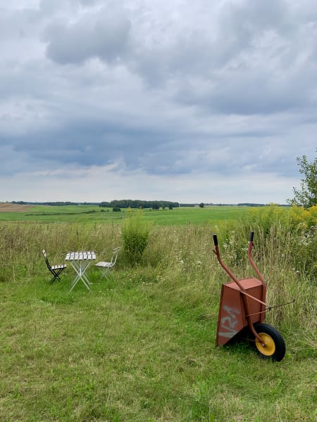 Turned over red wheelbarrow and a little picnic table and chairs in a green field, Mazury