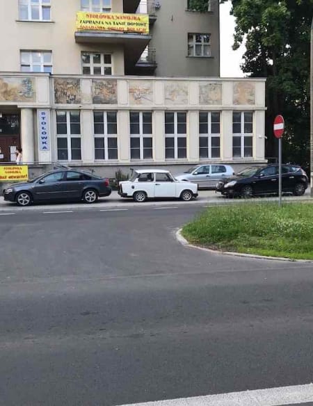 Photo of a tiny the most perfect maybe 1960s white car facing with its nose right in between two new silver cars with their noses facing left. Me against the world.