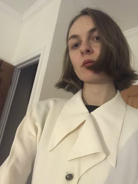 Selfie from below. Hair cut in bob to jawline. Wearing cream poet-type blouse with large wing collar.