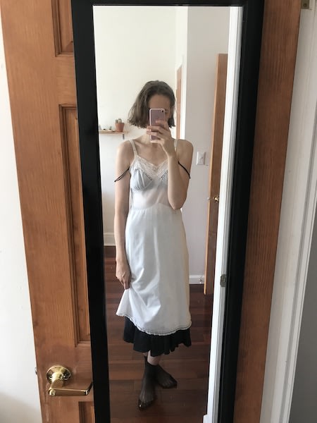 Mirror selfie wearing black mesh ankle socks, long black skirt and black bra with straps hanging down, and semi-sheer white cotton slip dress layered over top.