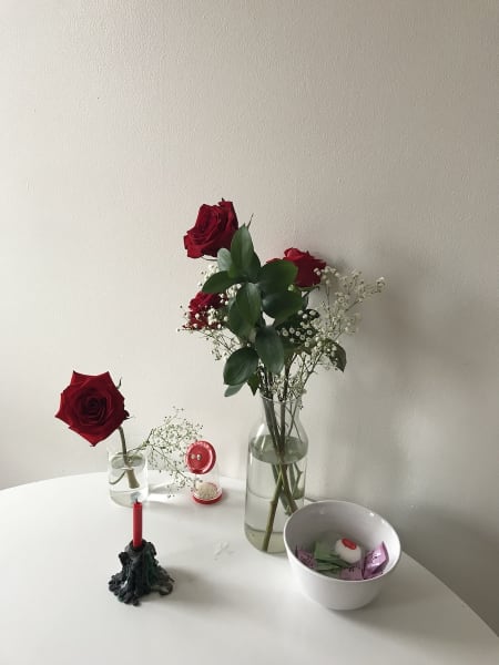 Red roses, candle, candies on a white tabletop.