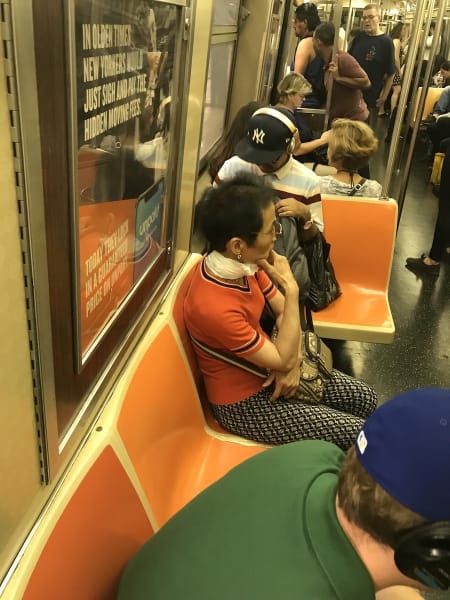 On a NYC subway car with orange seats, a person wears a generic plastic shopping bag as a scarf.