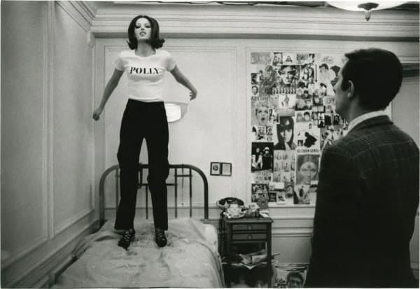 Black and white image of girl jumping on a bed in a shirt that says POLLY