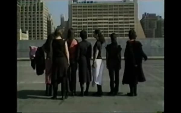Screenshot from BLESS video showing a group of people facing away from camera wearing black