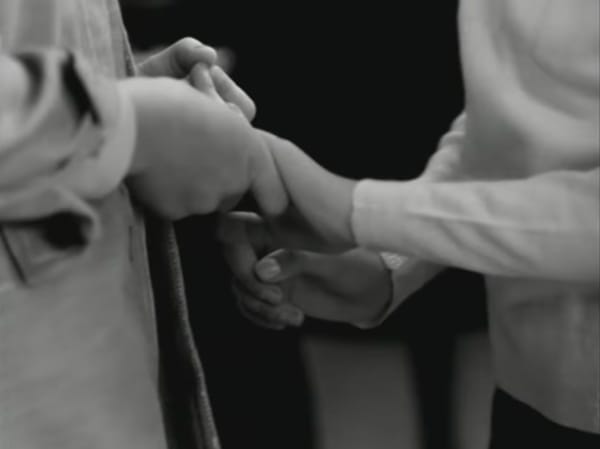 B&W screenshot from Kieslowki's film Siedem kobiet w różnym wieku, showing two people in close up holding hands