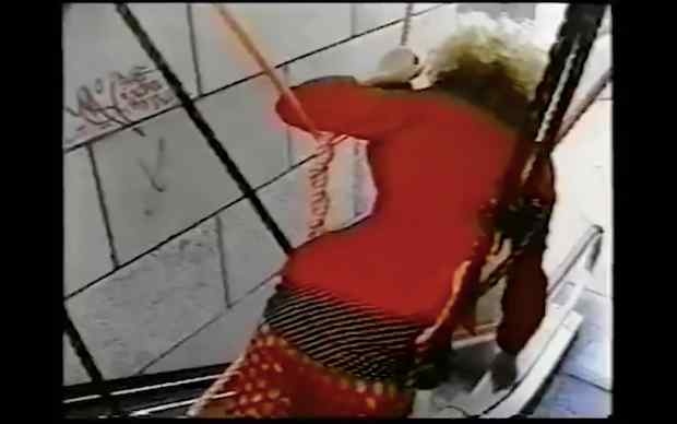 From Susan Cianciolo's Films and Collaborations 1996-2012, a woman in a long red dress? or red outfit with some black details lies face down in a kind of rope structure or hammock