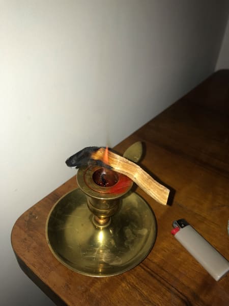 Stick of palo santo resting on red candle alight