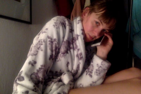 Photobooth photo of me wearing my white and purple-flower fleece robe leaning away from the camera in partial-profile while talking on my iPhone