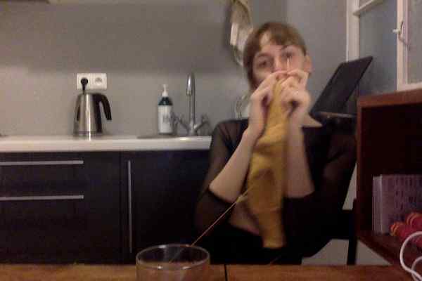 Photobooth picture of me at wooden table in a black mesh top holding up my yellow sock knitting a bit blurred coz a bit drunk