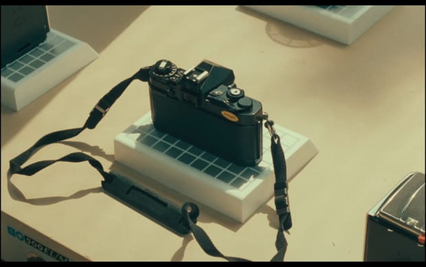 Robert Bresson - L'argent (1983), pretty black photo camera seen on display from behind