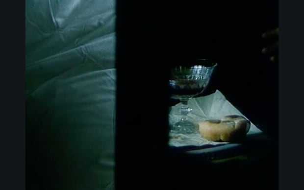Věra Chytilová - Fruit of Paradise (1970), a dark room a bit green-lit showing a bułka and glass on a side table
