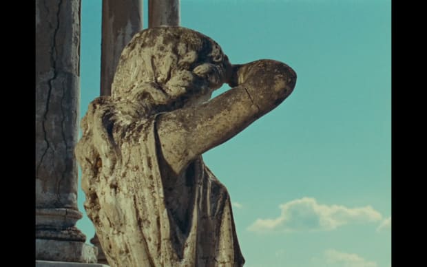 Agnès Varda - Along the Coast (1958), back of a stone grecian statue woman against summer blue sky