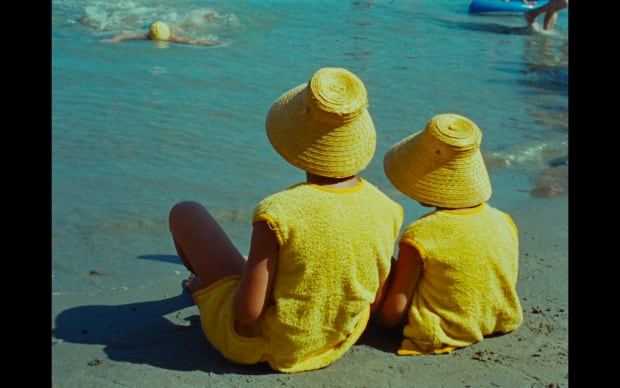 Agnès Varda - Along the Coast (1958), adult and child pictured from behind wearing matching yellow sun hats and yellow terrycloth cover up