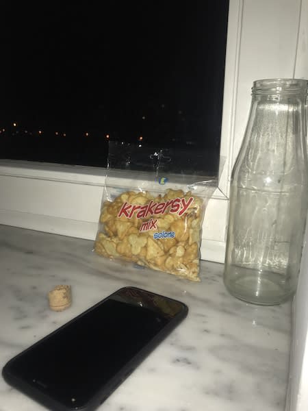 Bag of crackers and iphone and half a cork and a glass bottle on a windowsill at night
