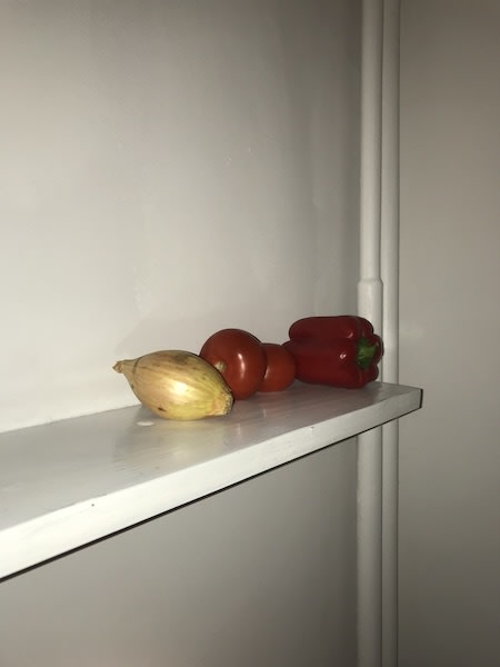 An onion, two tomatoes and a red capsicum on a white shelf