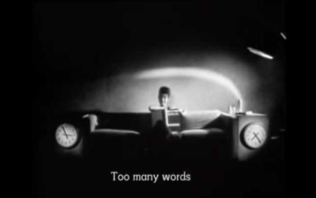 Black and white screenshot from the film Ghost Dance showing a woman sitting on a couch, with subtitle Too many words
