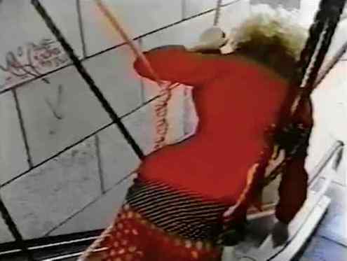 Screenshot from Susan Ciancolo film, very lo-fi video, showing a woman in a red dress draped strangely in what seems to be a harness or rope structure, we see her from behind as if she has fallen in