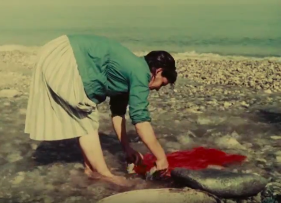 A woman washing a red garment in a rock pool near the sea, from Vittorio de Seta's The Age of Swordfish