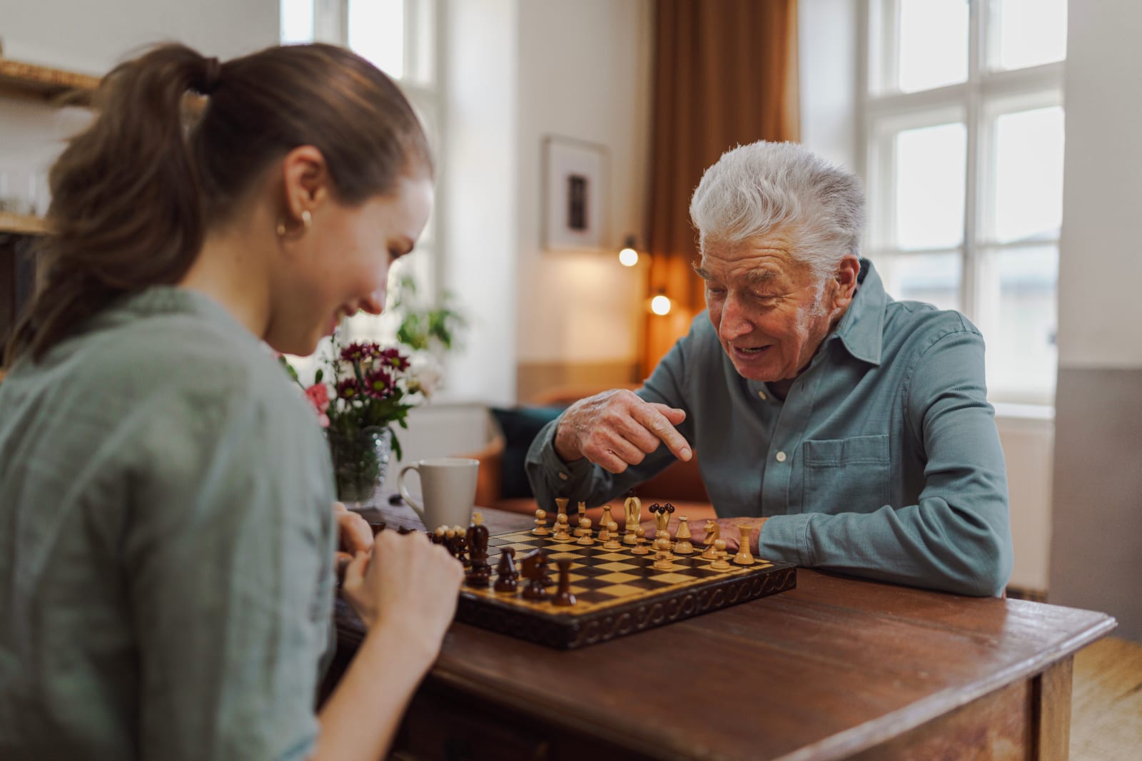 Younger woman and elderly grandfather playing chess together at home