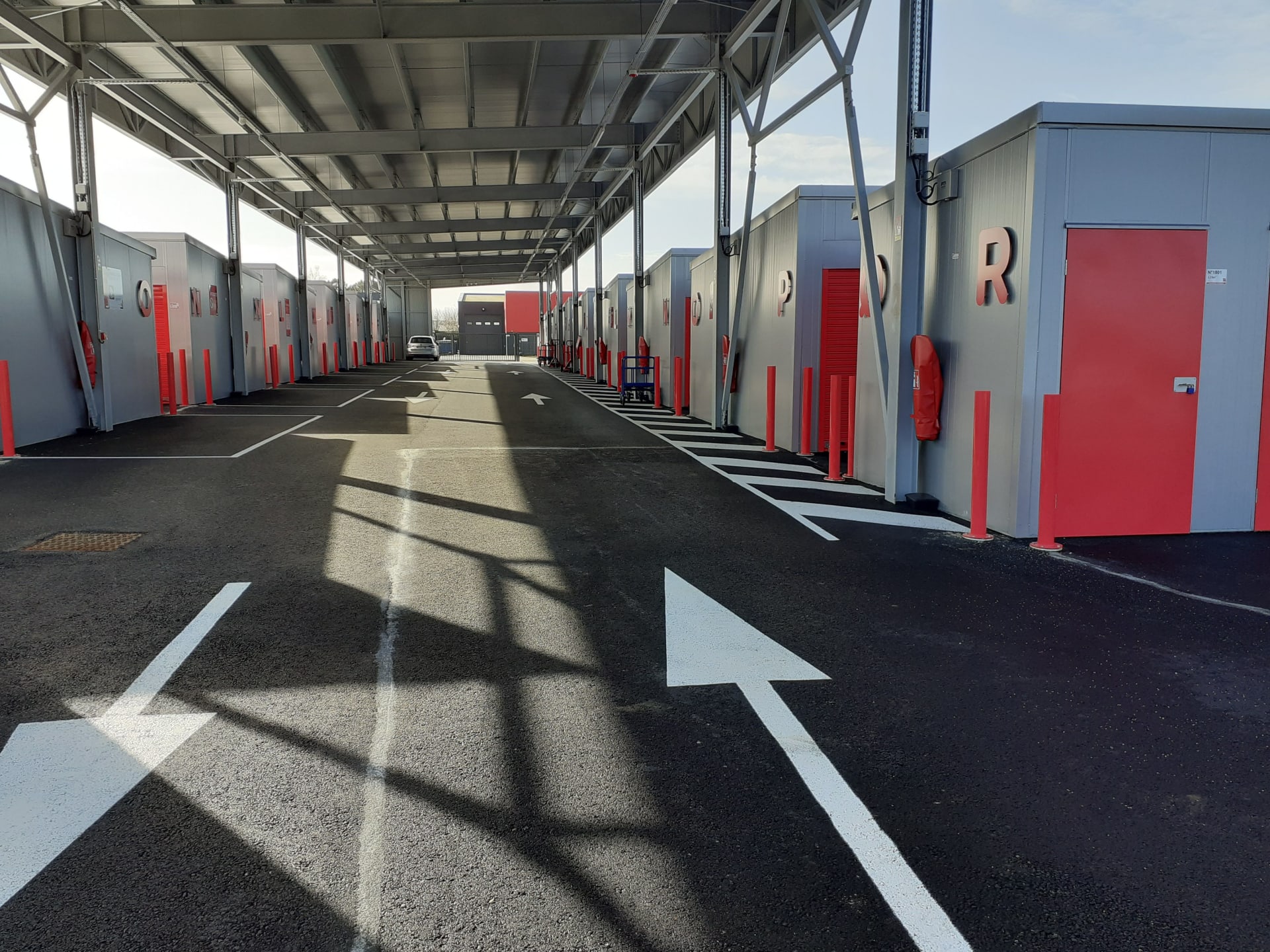 Outdoor covered drive-through alley with red storage unit doors and directional arrows at HOMEBOX Vannes Sud, Allée Nicolas Appert - ZA du Prat, Vannes