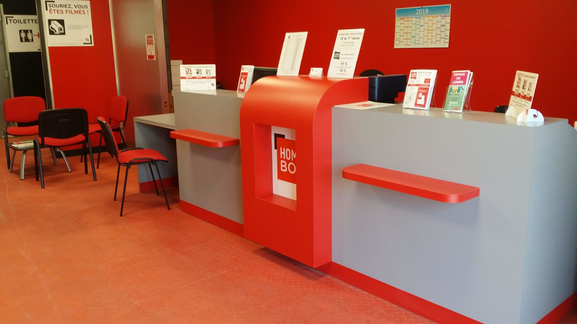 Comptoir d'accueil rouge avec chaises et présentoirs documentaires du centre HOMEBOX Romilly-sur-Seine