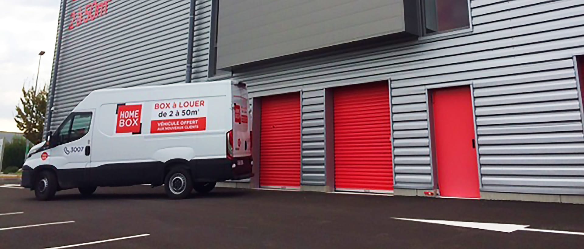 Utilitaire HOMEBOX garé devant des portes de box rouges sur la façade d’un centre HOMEBOX.
