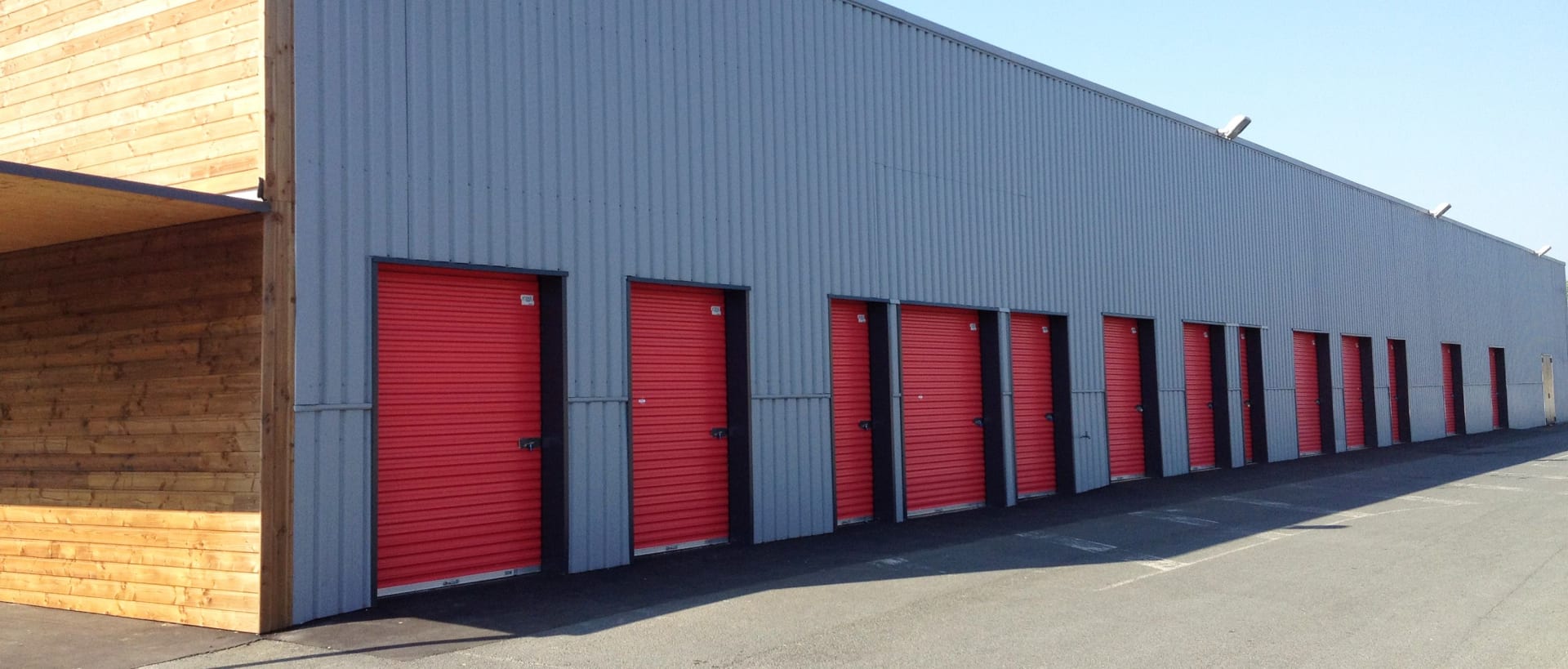 Long grey warehouse exterior with row of red storage doors and wooden canopy at HOMEBOX Cholet, 12 avenue de la Marne, Cholet
