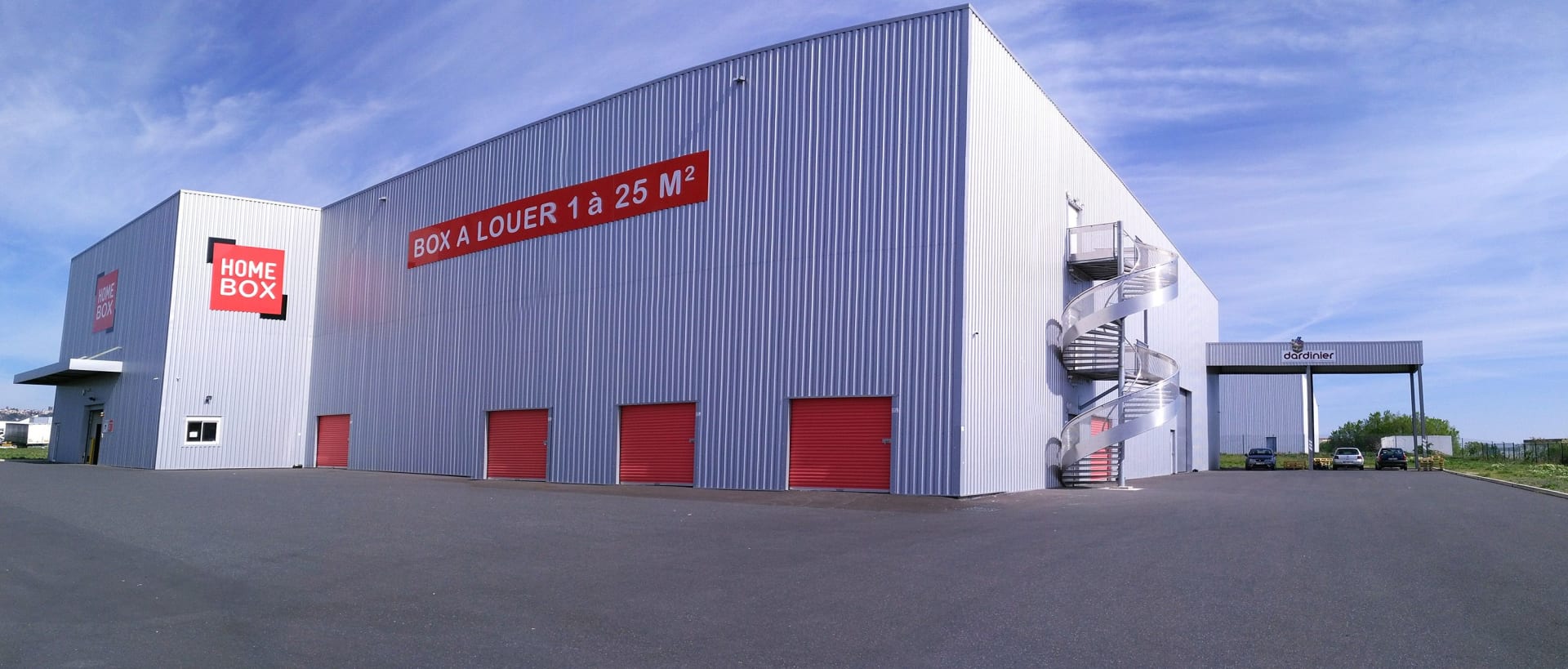 Vue extérieure du bâtiment HOMEBOX Cébazat avec plusieurs box accessibles et large parking.