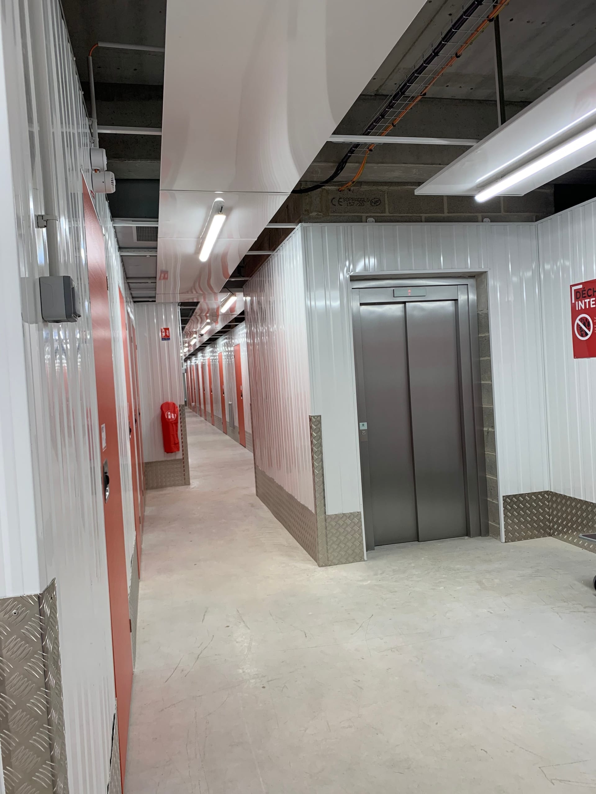 Couloir intérieur du centre HOMEBOX Amiens - Glisy avec ascenseur et portes de box rouges.